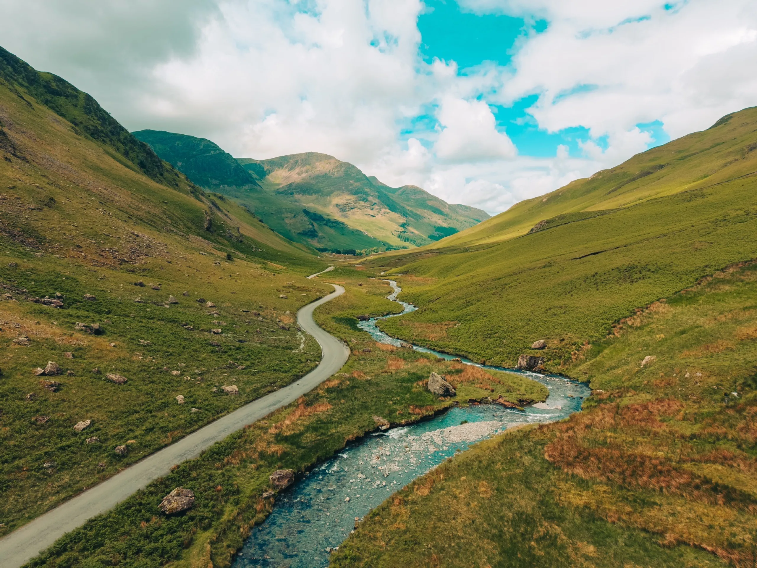 A winding road and river run through a green mountain valley.